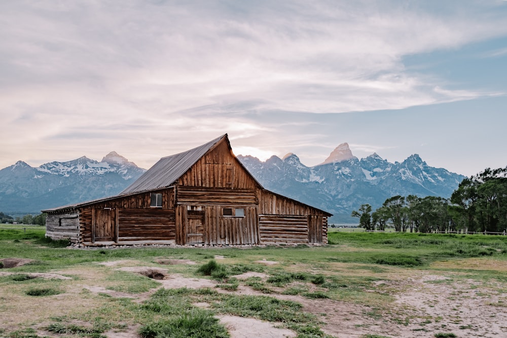 brown wooden house on green grass field near mountains under white clouds during daytime