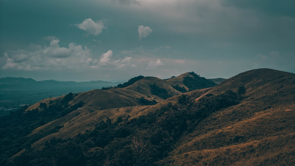 Montañas marrones y verdes bajo nubes blancas y cielo azul durante el día