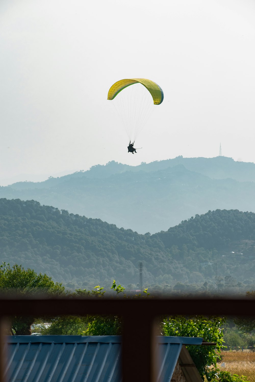 person riding yellow parachute over green mountains during daytime