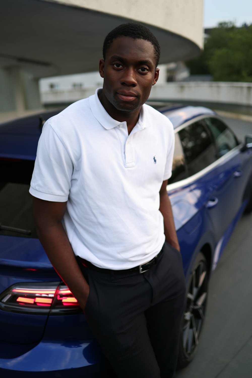 man in white polo shirt standing beside blue car