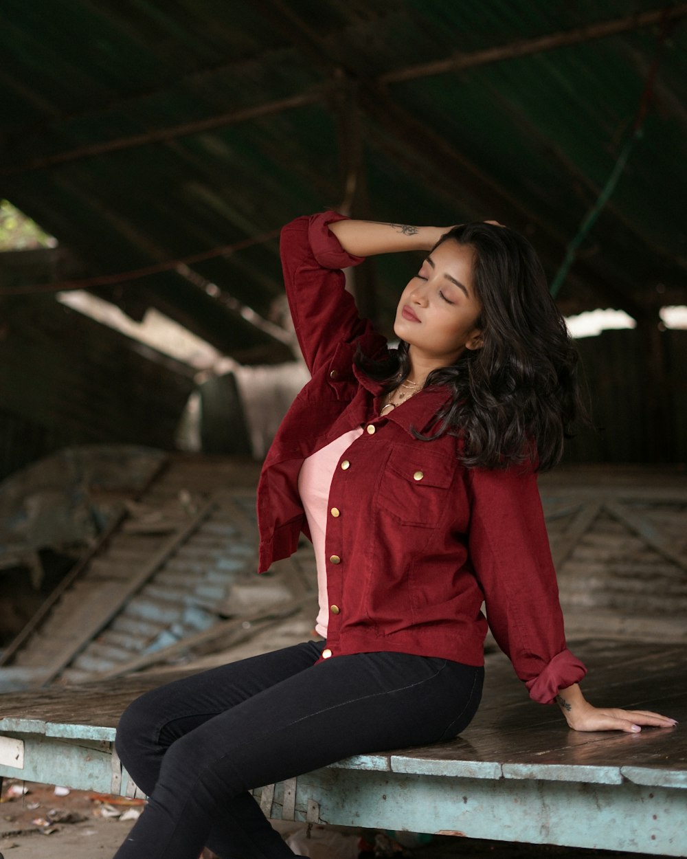 woman in red button up long sleeve shirt and black pants sitting on brown wooden dock
