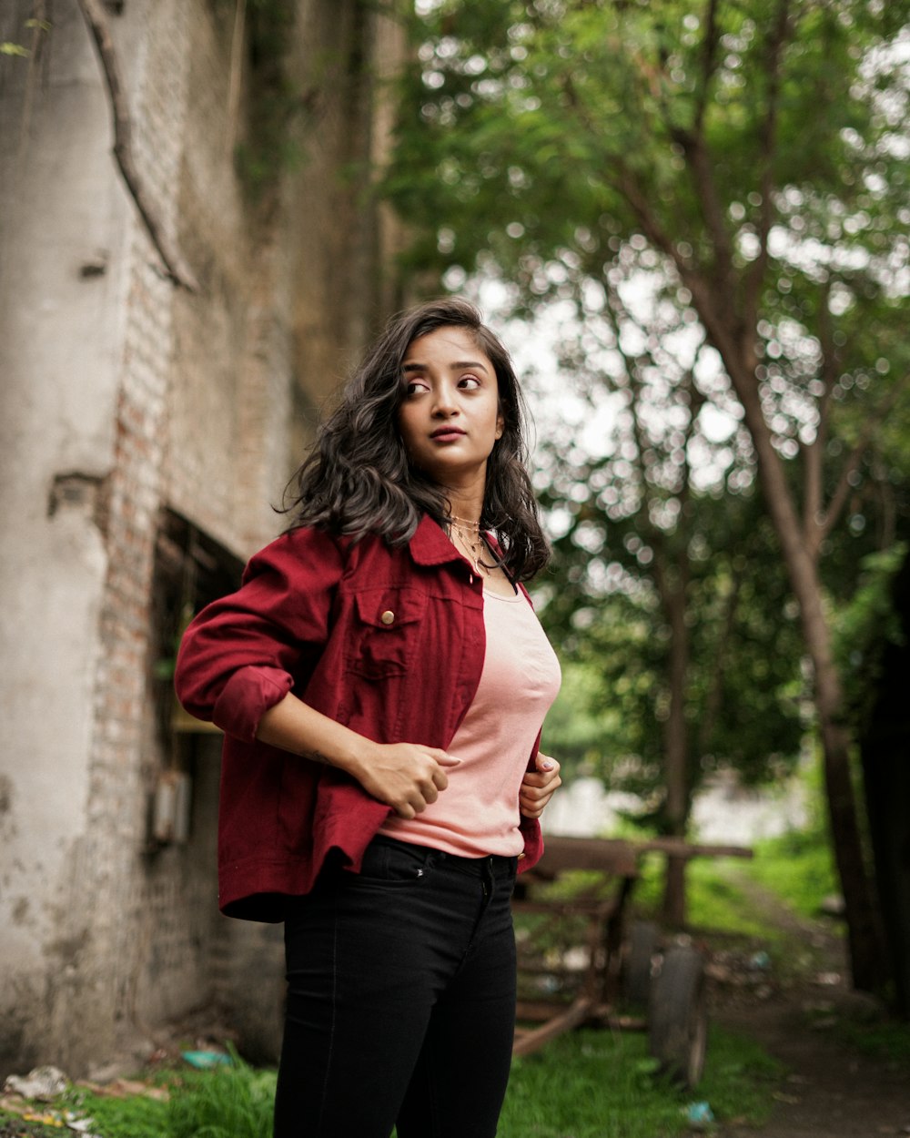 woman in red dress shirt and black pants standing near tree during daytime