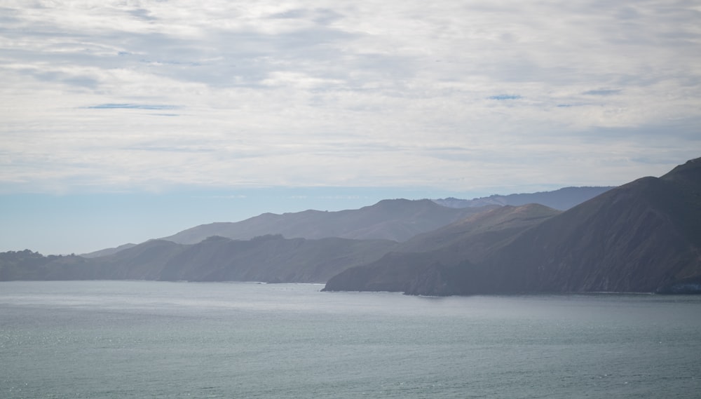 montagnes vertes à côté du plan d’eau sous des nuages blancs pendant la journée