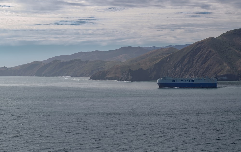 navio azul e branco no mar perto da montanha sob nuvens brancas durante o dia