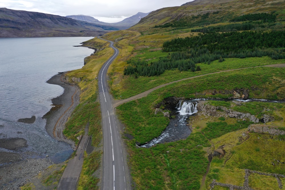 gray concrete road near green grass field and body of water during daytime