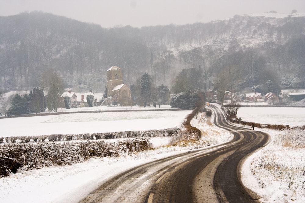 gray road in between snow covered field during daytime