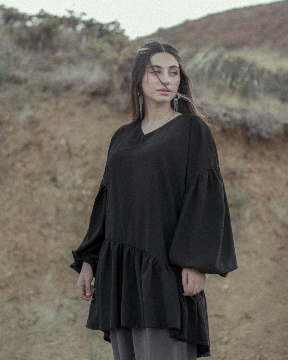 Femme en robe noire à manches longues debout sur le champ d’herbe brune pendant la journée