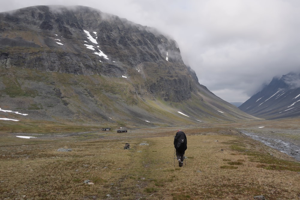 person walking on green grass field near gray mountain during daytime