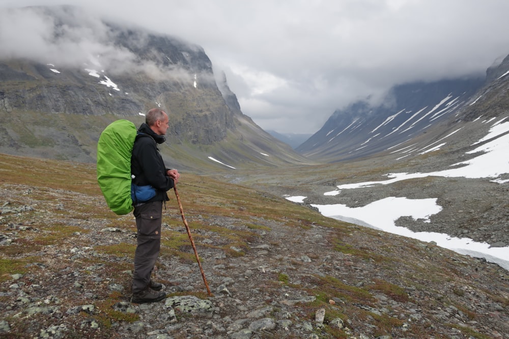 man in green jacket and black pants holding red stick standing on rocky ground