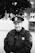 A calm, professional law enforcement officer in uniform, standing confidently outdoors with a subtle blue line flag in the background.