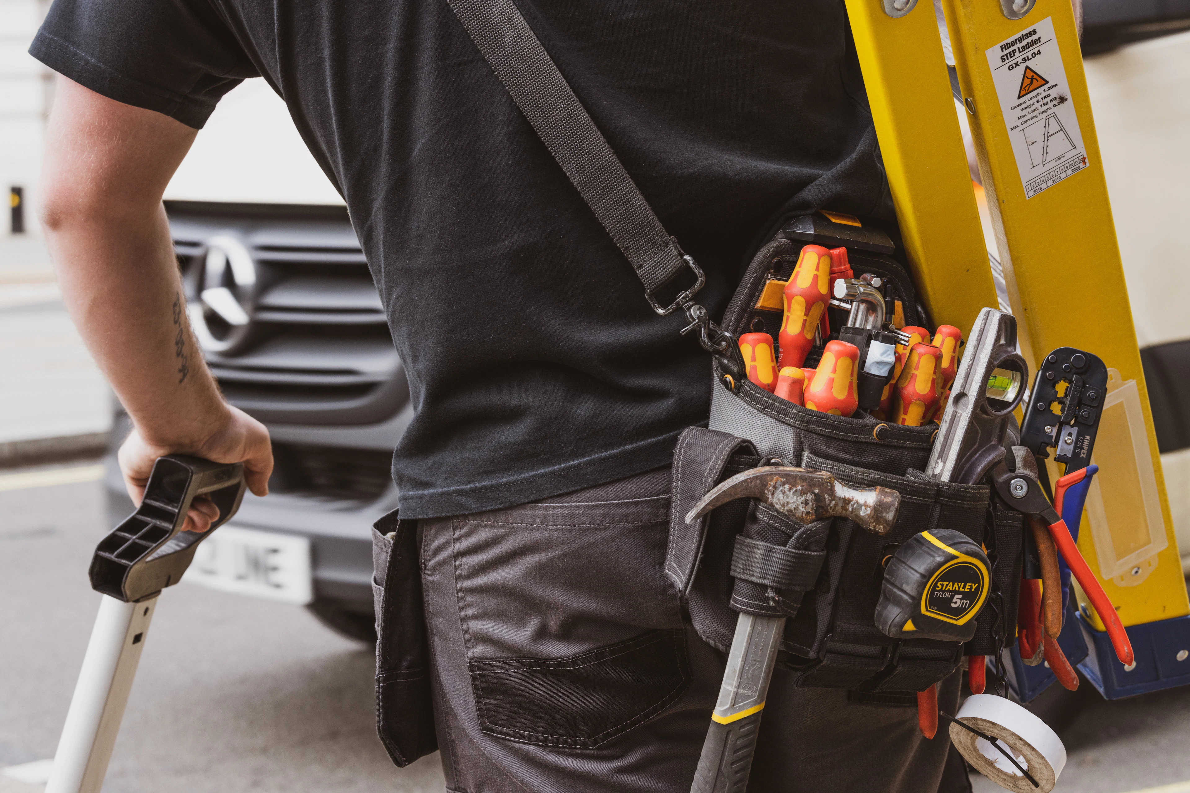 Technicien et sa ceinture à outils devant son utilitaire