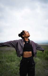 woman in black crop top and black denim jacket standing on green grass field during daytime