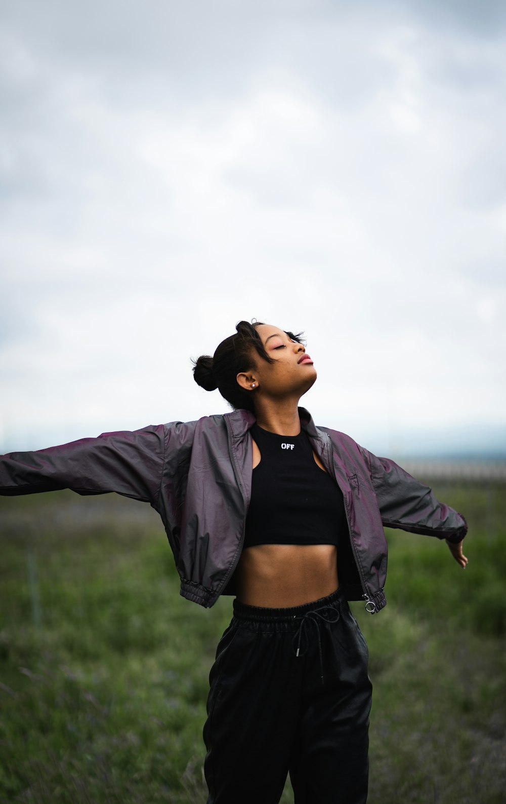 woman in black crop top and black denim jacket standing on green grass field during daytime