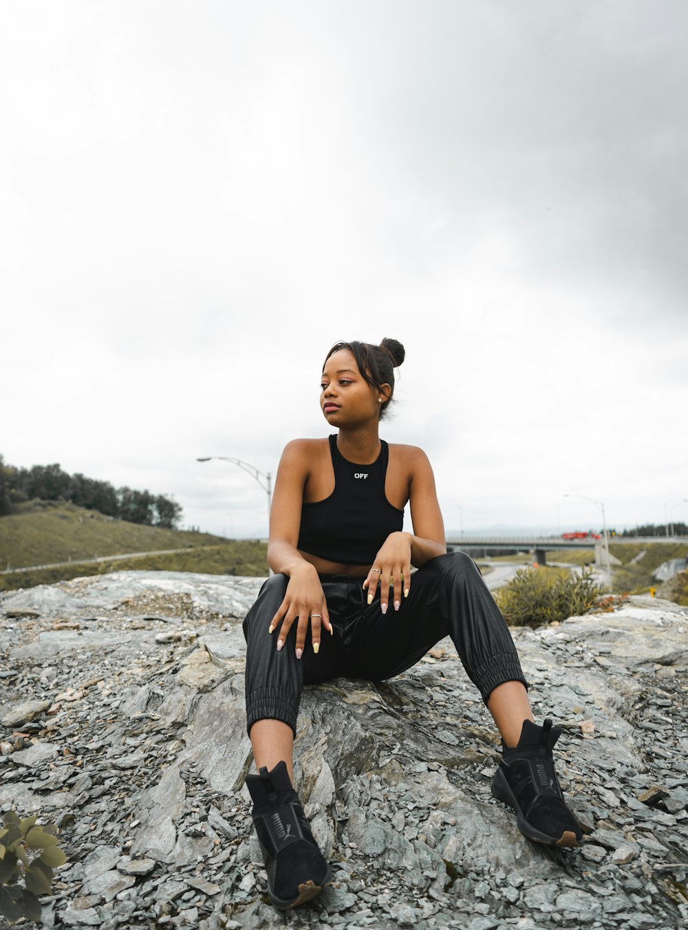 woman in black tank top and black pants sitting on rock during daytime
