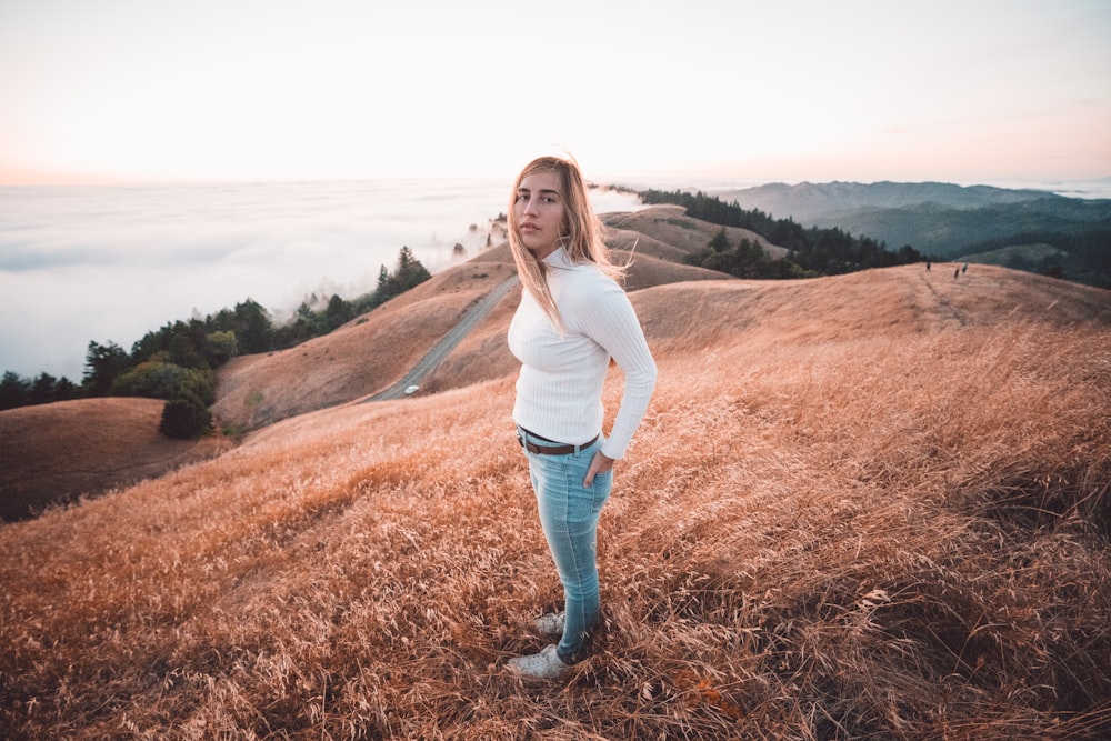woman in white long sleeve shirt and blue denim jeans standing on brown grass field during