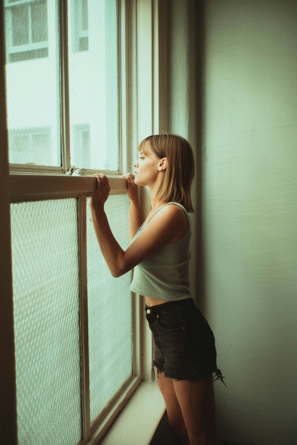 woman in white tank top and black denim jeans standing beside window