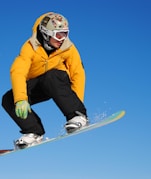 man in yellow jacket and blue pants riding on white snowboard