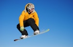 man in yellow jacket and blue pants riding on white snowboard