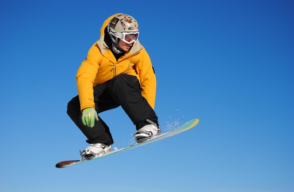 Hombre con chaqueta amarilla y pantalones azules montando en una tabla de snowboard blanca