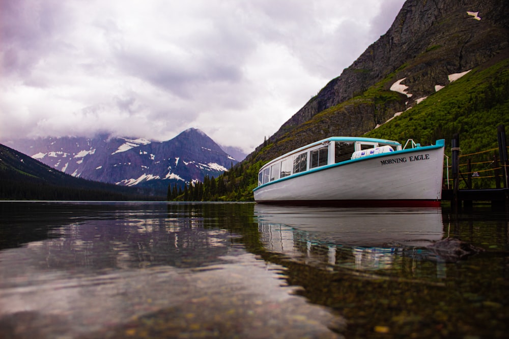 white and blue boat on lake near mountain under cloudy sky during daytime