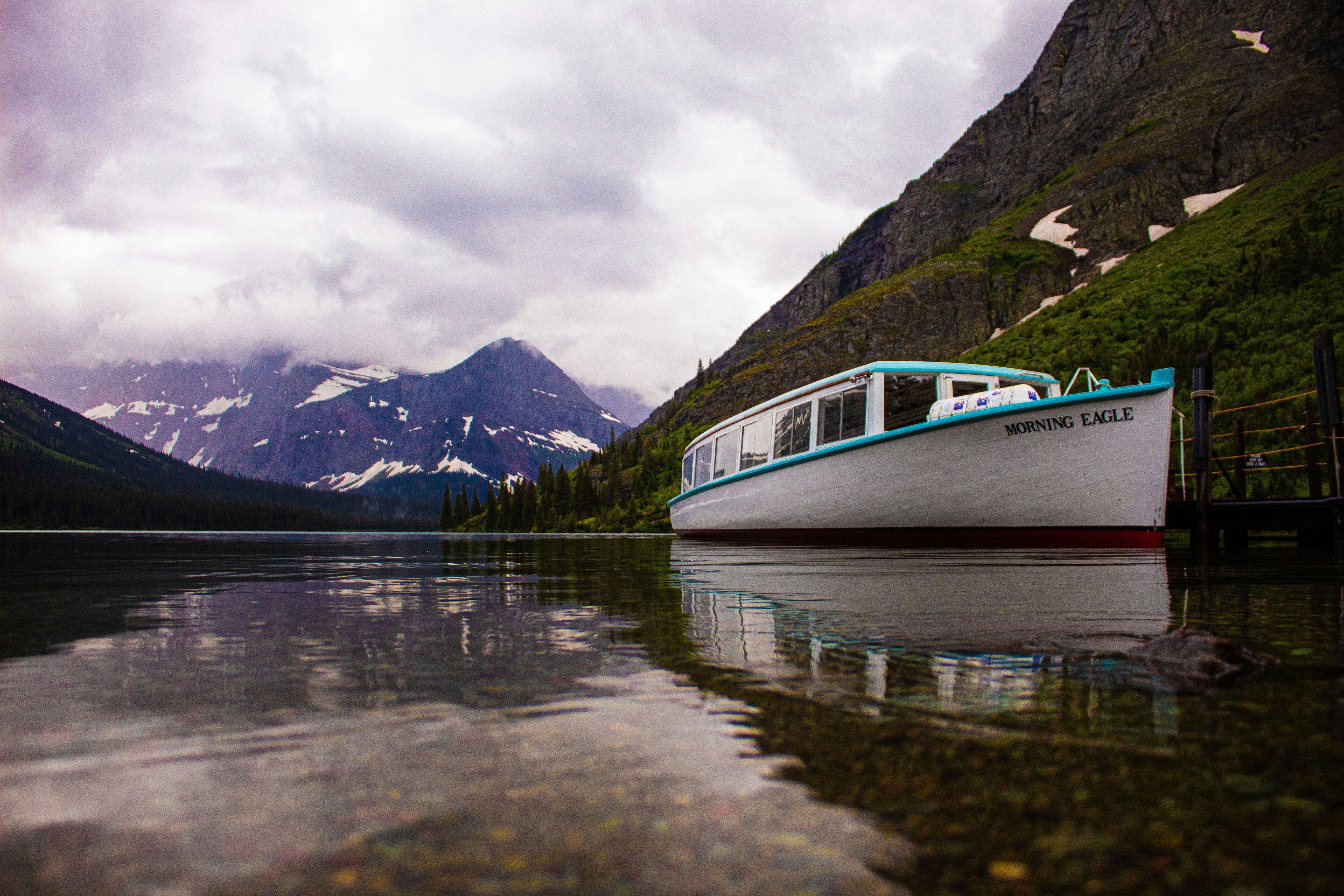 white and blue boat on lake near mountain under cloudy sky during daytime