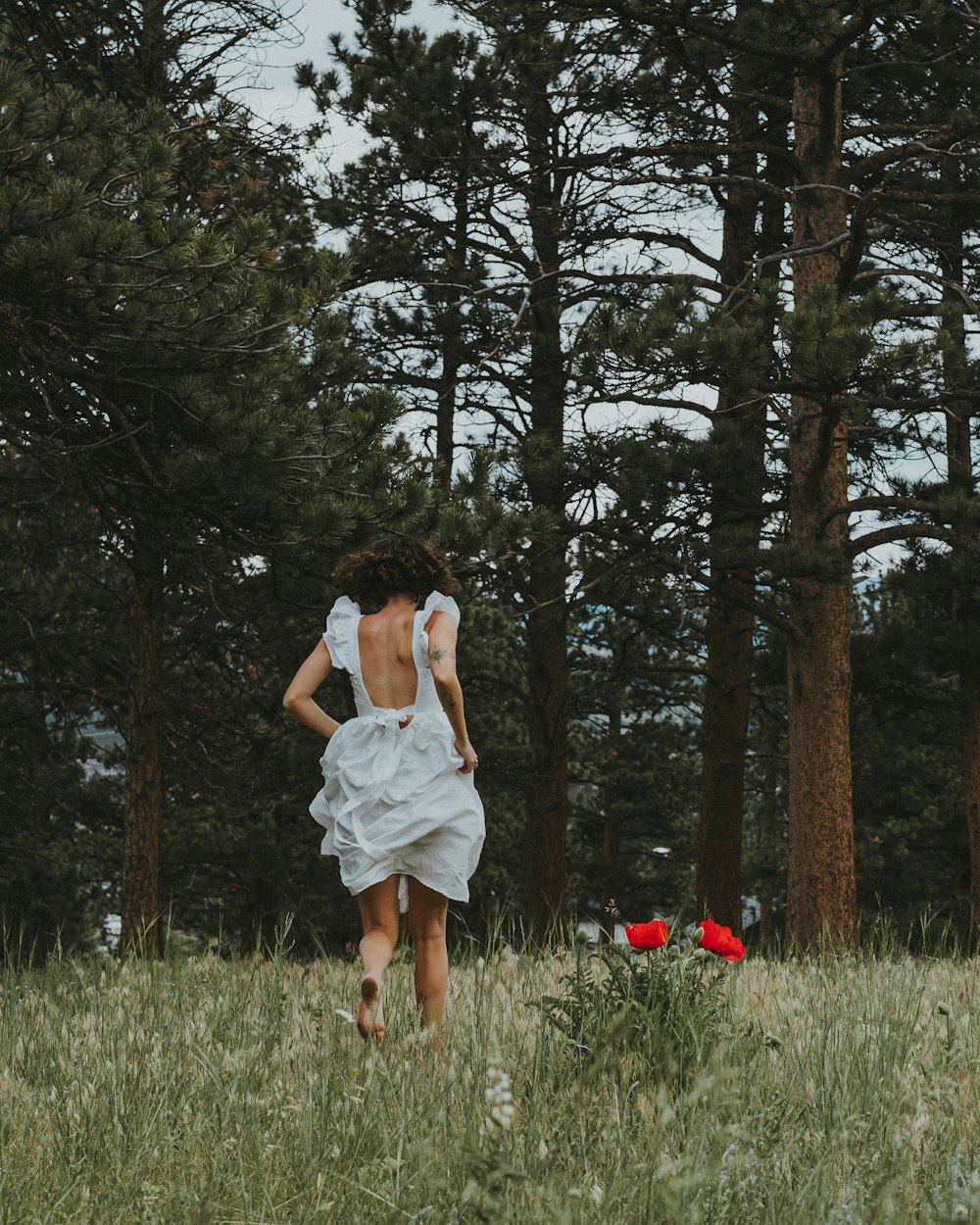 femme en robe blanche debout sur le champ d’herbe verte pendant la journée