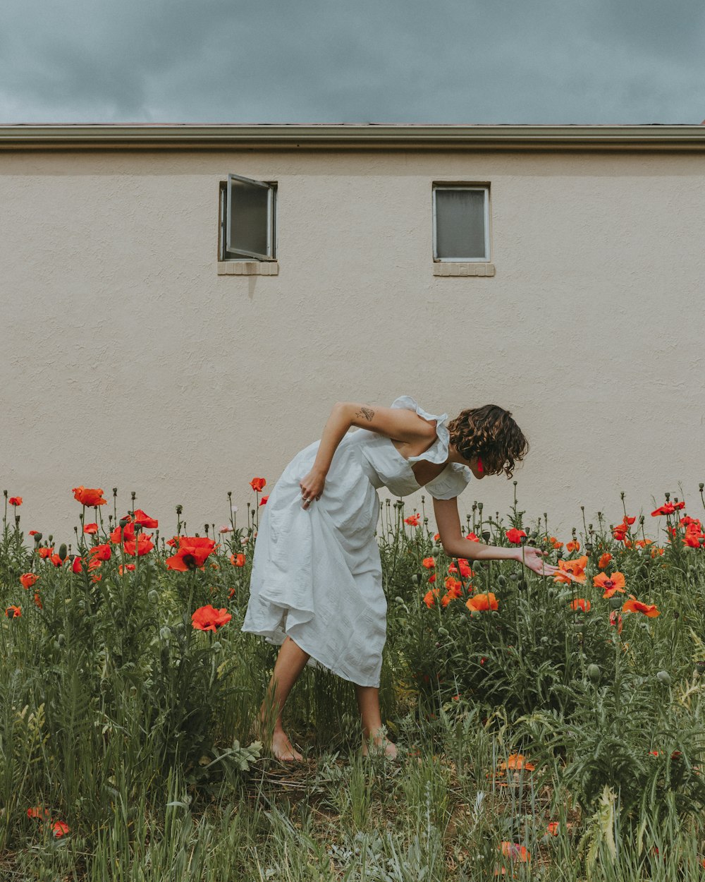 woman in white dress standing on red flower field during daytime