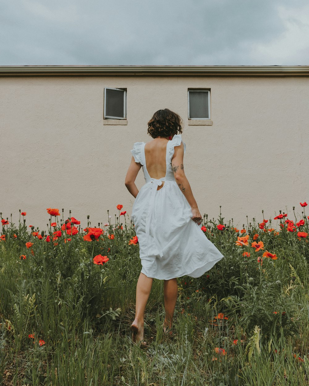 Femme en robe blanche debout devant des fleurs rouges