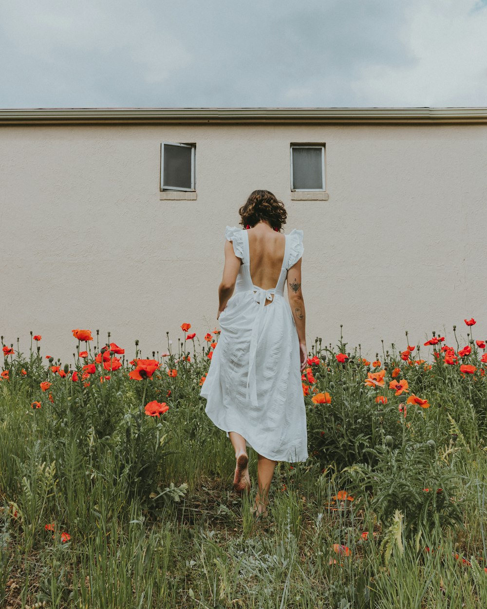 woman in white dress standing in front of red flowers