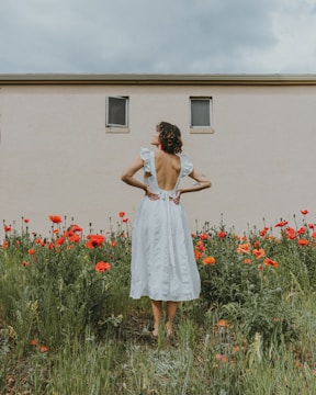 woman in white dress standing on red flower field during daytime