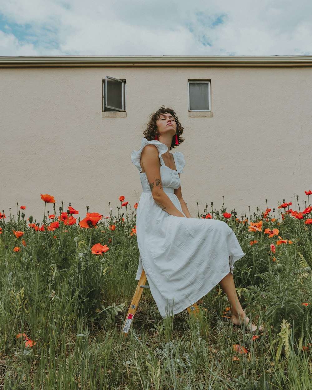 donna in vestito bianco che si siede sul campo di fiori rossi durante il giorno