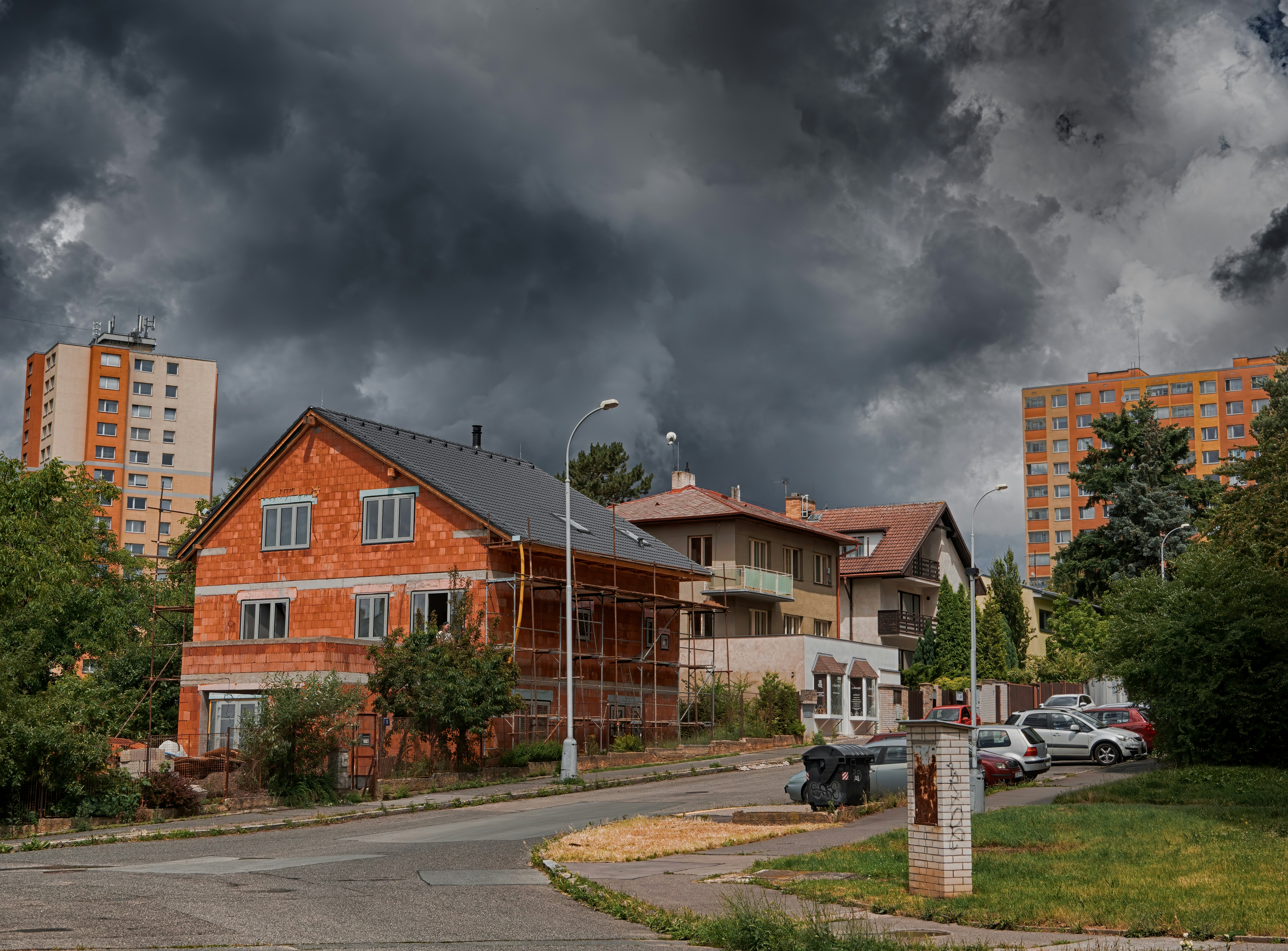cars parked on side of the road near houses under gray cloudy sky