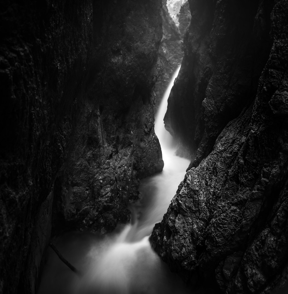 grayscale photo of waterfalls between rocky mountain