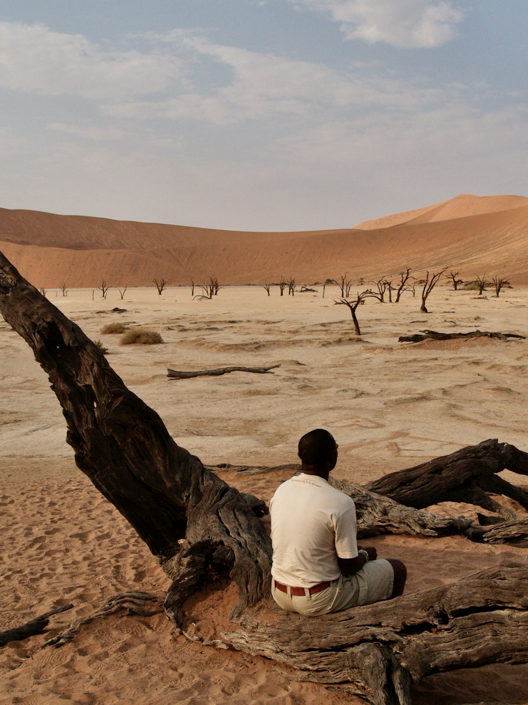 man in white shirt sitting on brown sand during daytime