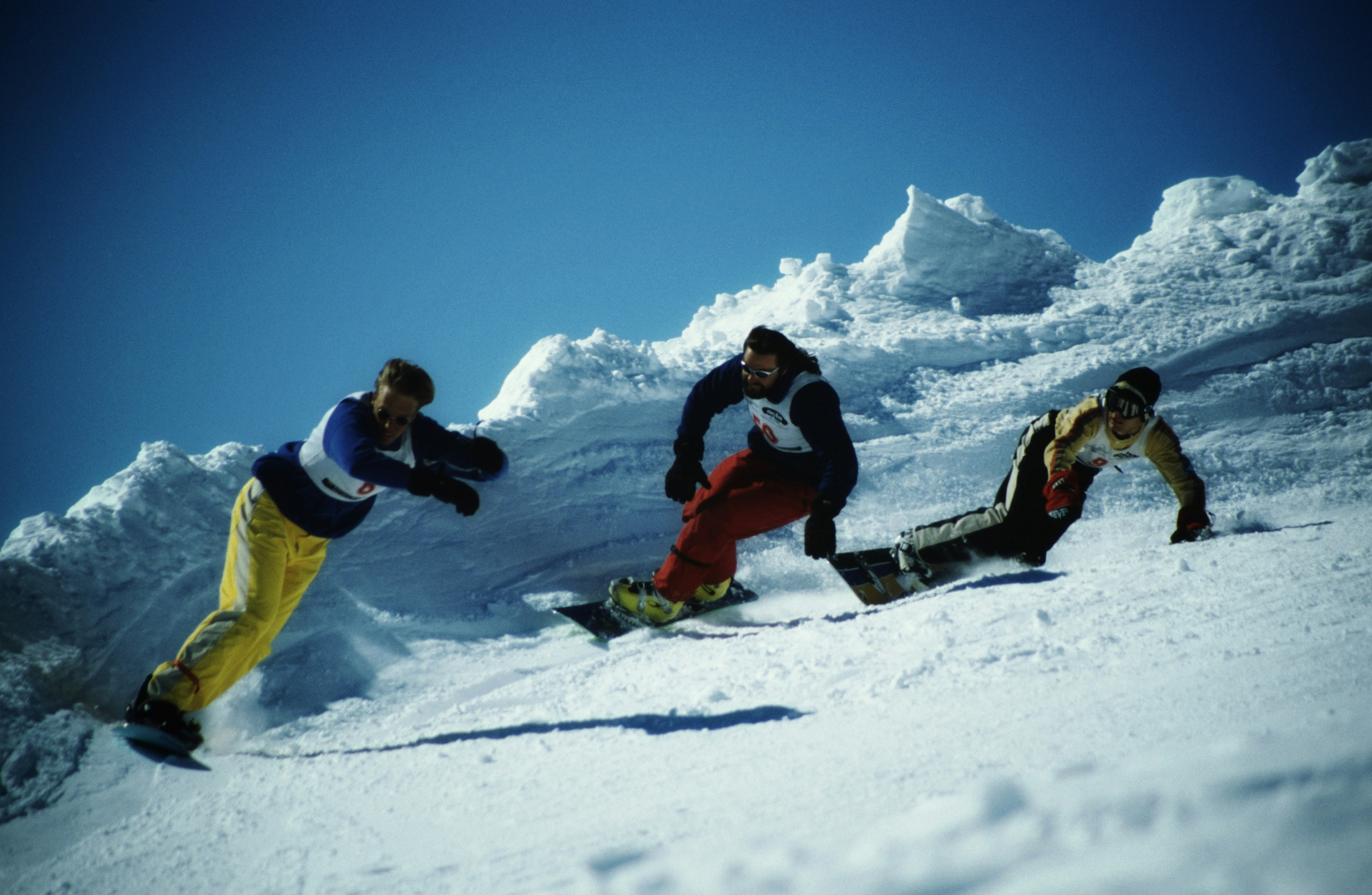 2 men in red and yellow jacket and black pants riding on snowboard during daytime