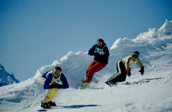 2 person in red and white snow suit riding on snow board during daytime