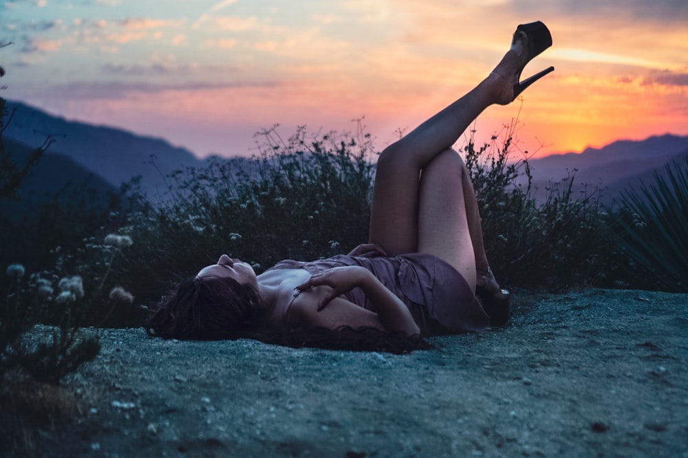 woman lying on white textile on body of water during sunset