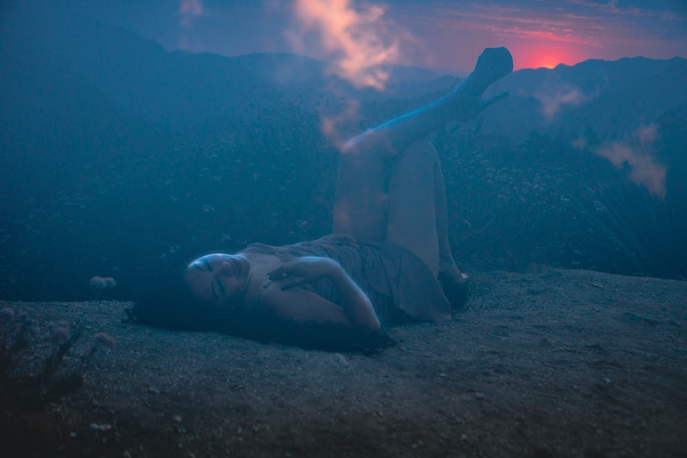 woman in white tank top and white shorts lying on ground with blue smoke