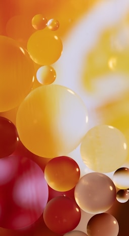 Multicolored translucent spheres in varying shades of yellow, orange, and red appear against a softly lit background. The spheres overlap and interact with light, creating a sense of depth and fluidity.