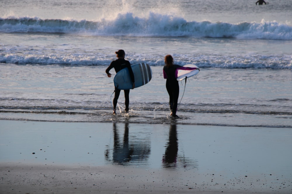 man holding white surfboard walking on seashore during daytime