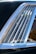 A close-up view of a car window with several vertical metal slats inside the window frame. The chrome trim of the window reflects light, enhancing its shine. The interior of the car is partially visible through the slats, and there are subtle reflections on the glass surface.