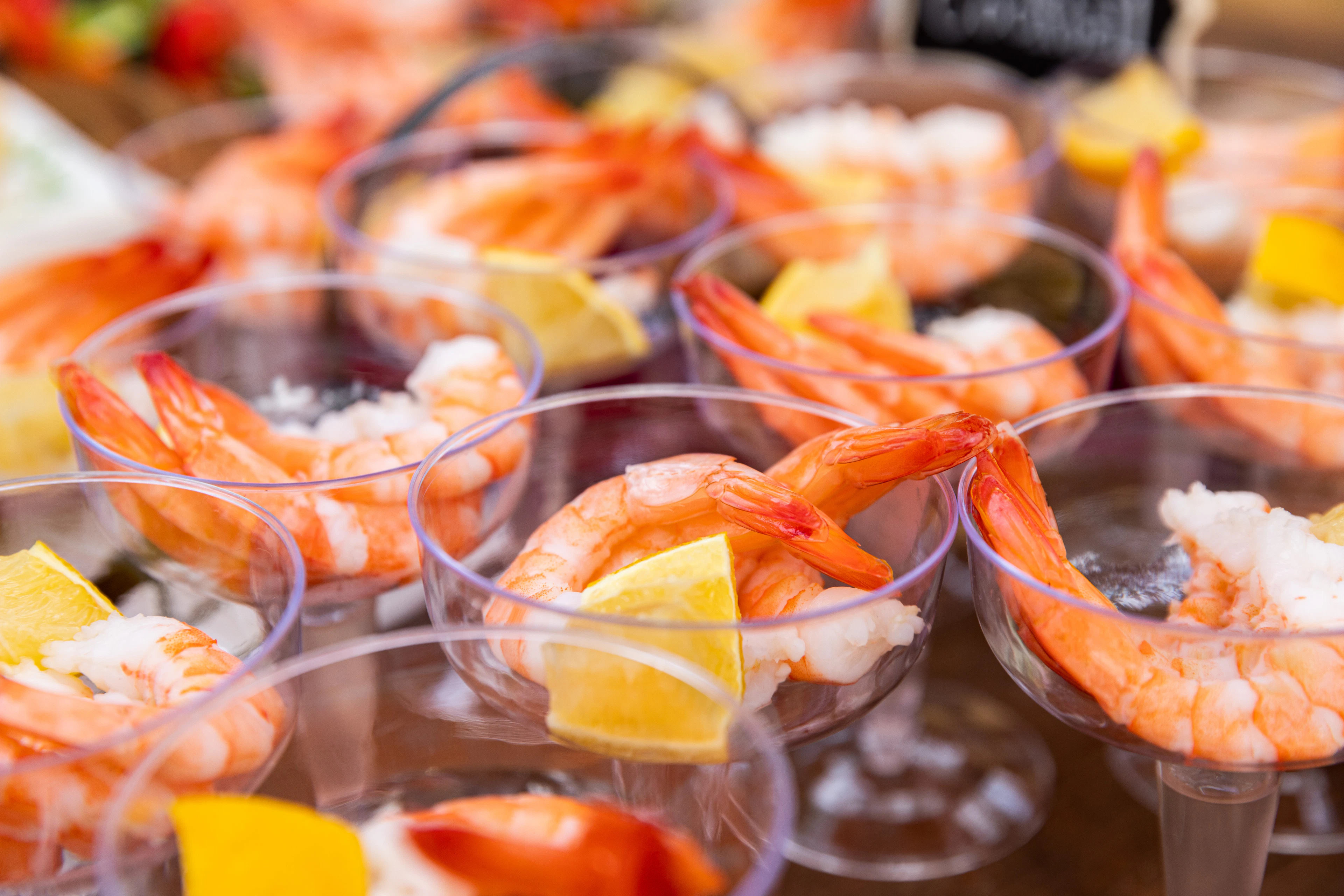 Rows of shrimp cocktail glasses with lemon, set out along a buffet counter