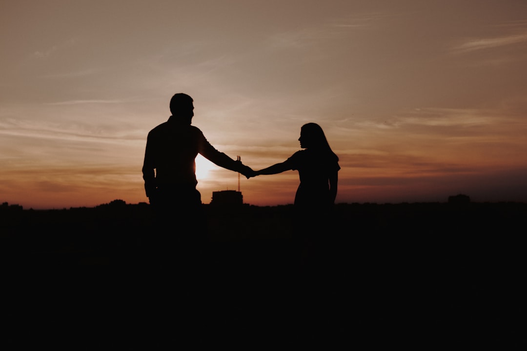 silhouette of man and woman standing on ground during sunset