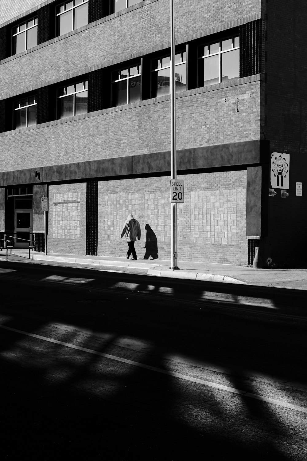 grayscale photo of man walking on sidewalk near building