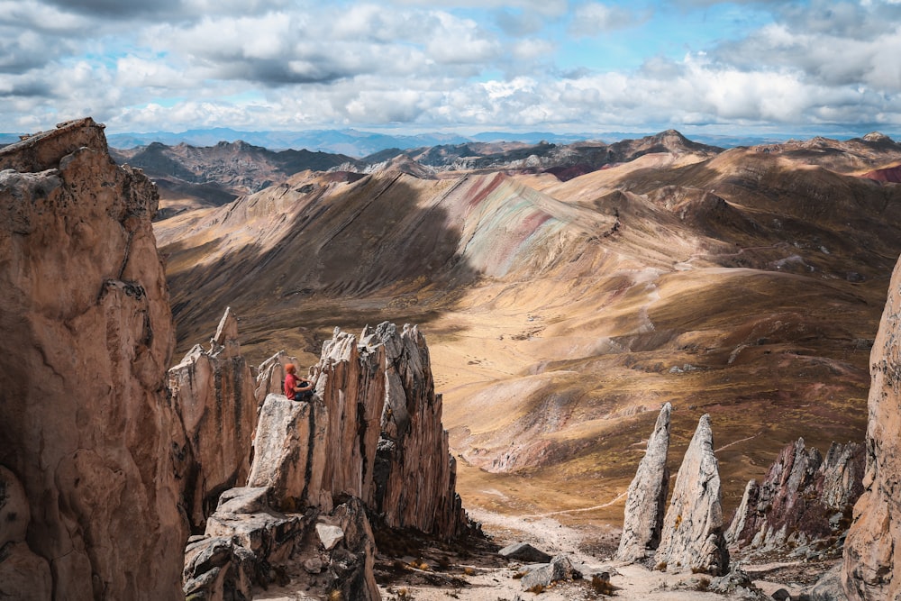 person in red jacket and black pants standing on brown rock formation during daytime