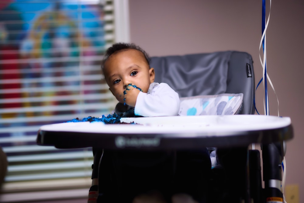 baby in white long sleeve shirt sitting on white high chair