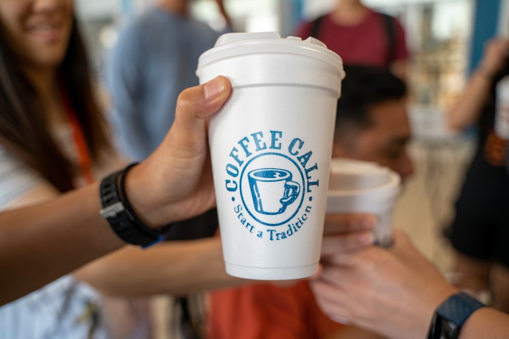 Persona sosteniendo un vaso desechable blanco y azul