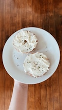 Close-up of a golden, toasted bagel resting next to cream cheese and fresh veggies on a rustic wooden table.