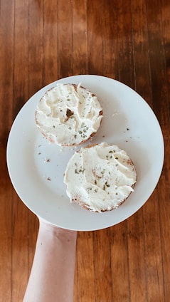 A warm, golden-brown bagel resting on a rustic wooden board with cream cheese and fresh herbs.