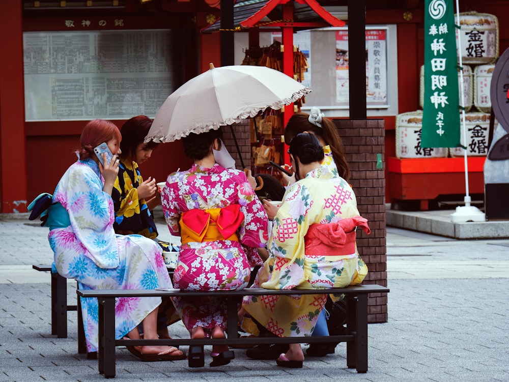 Frau im rosa Kimono sitzt tagsüber auf einer roten Holzbank mit Regenschirm